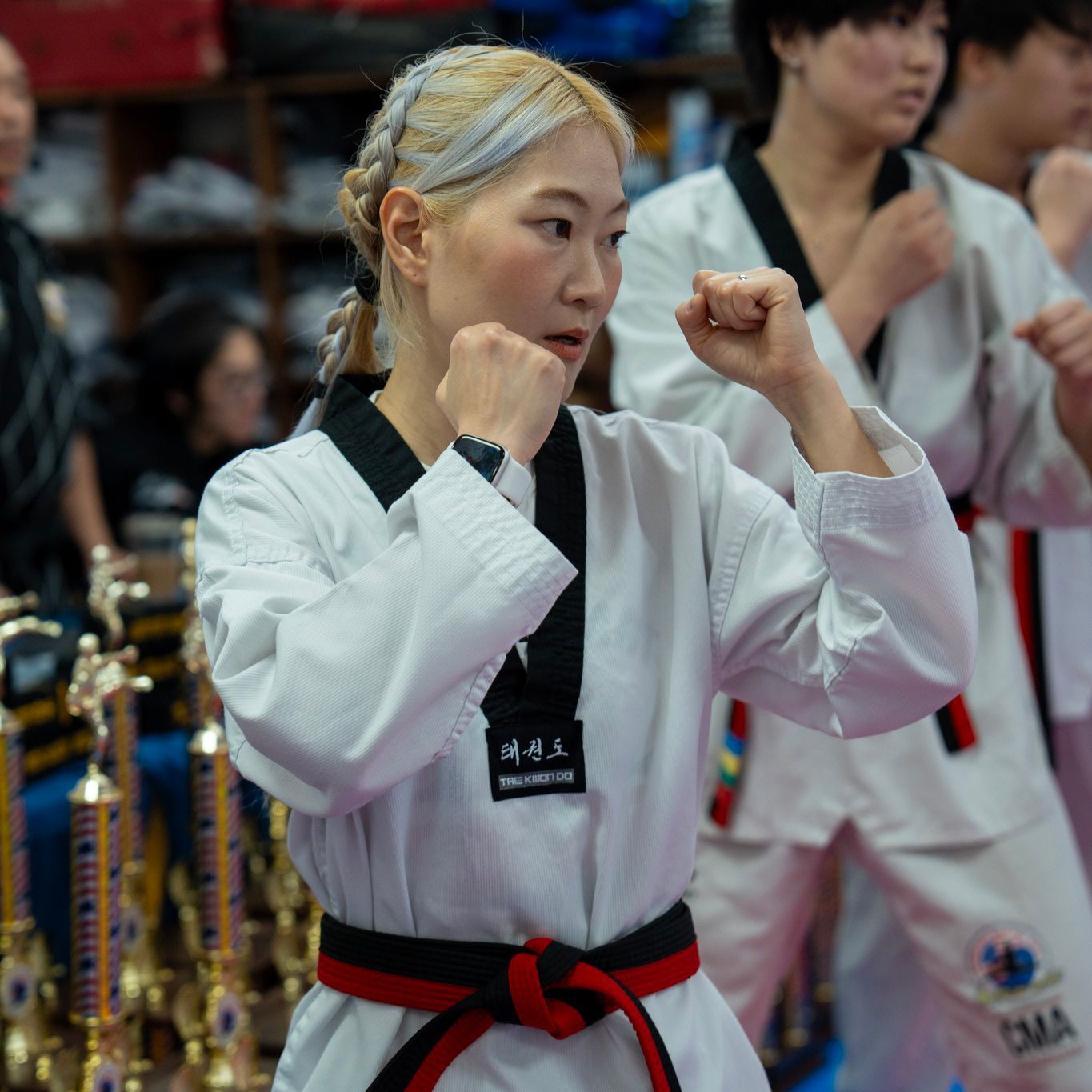 A woman in a taekwondo uniform is standing in front of trophies