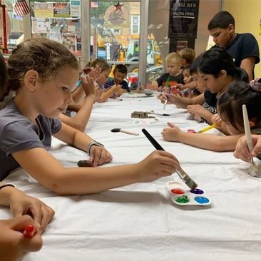 A group of children are sitting at a table painting with watercolors.