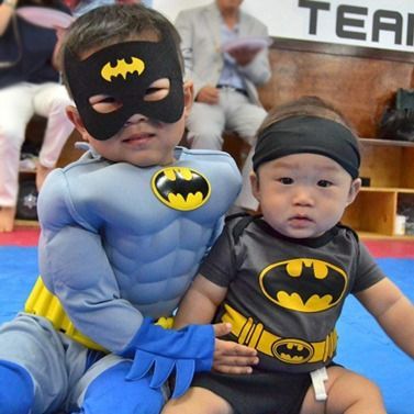 Two babies dressed in batman costumes are posing for a picture