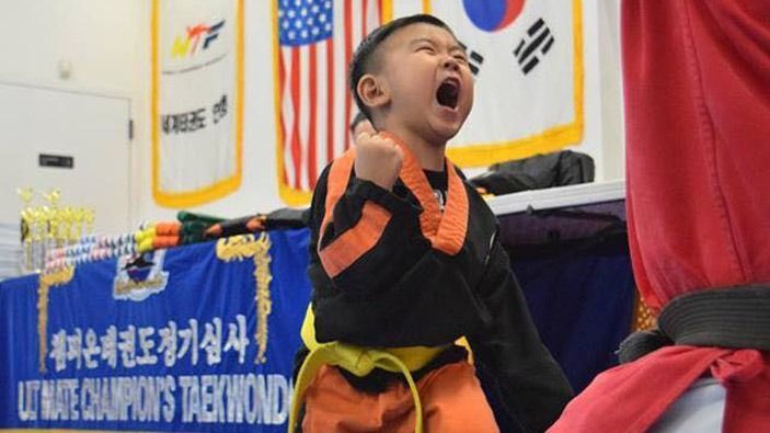A young boy in a taekwondo uniform holds his fist up in the air