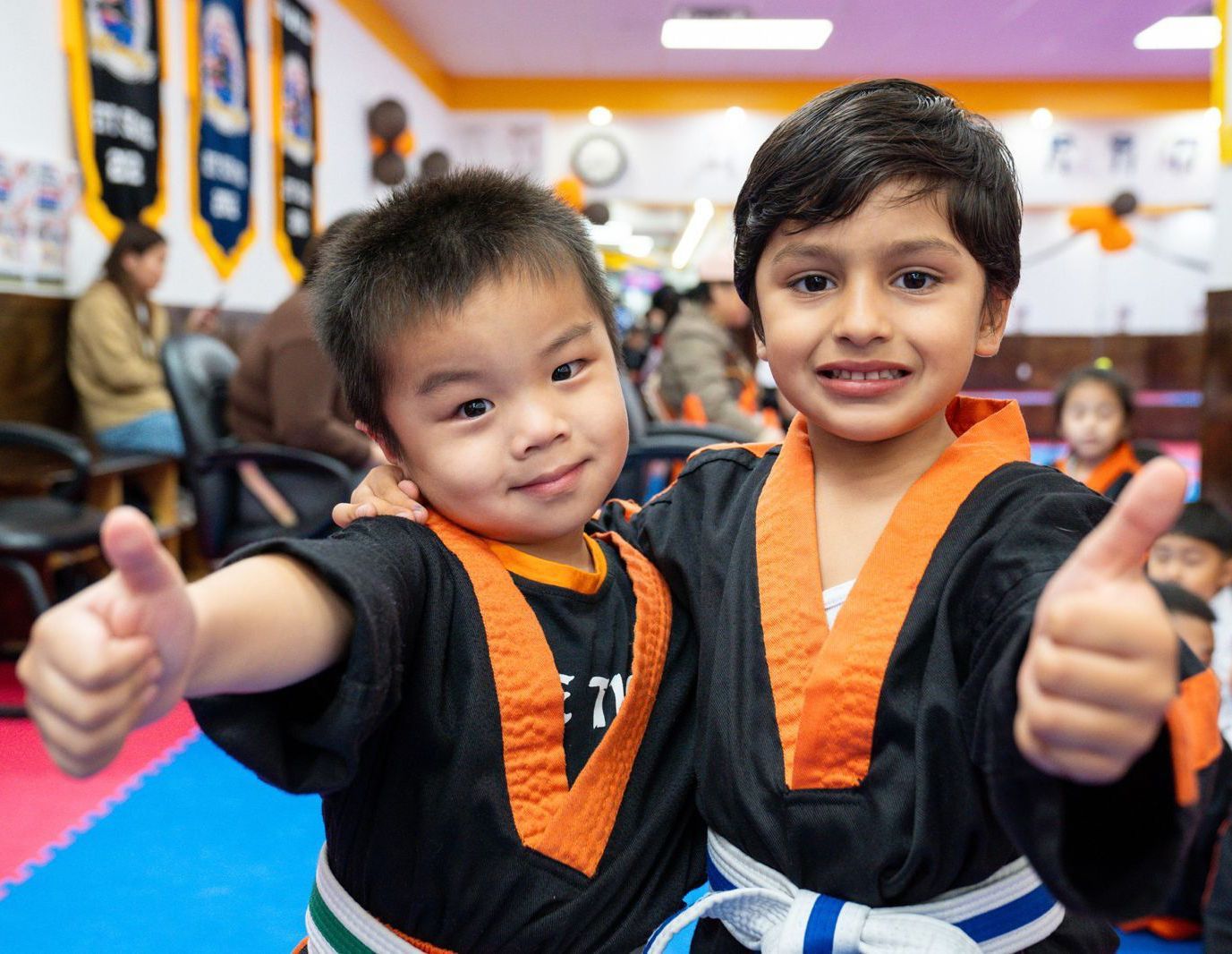 two young boys in karate uniforms are giving a thumbs up .