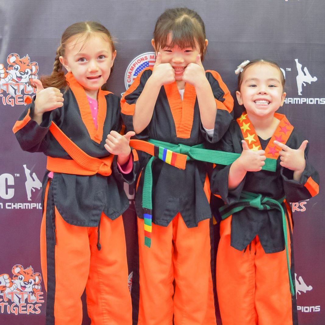 Three young girls are posing for a picture in front of a banner that says champions