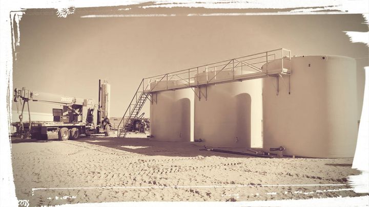 Oil storage tanks with a truck in a desert landscape, sepia tone.
