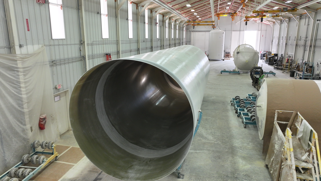 Large cylindrical structure inside a manufacturing facility with other equipment and windows.