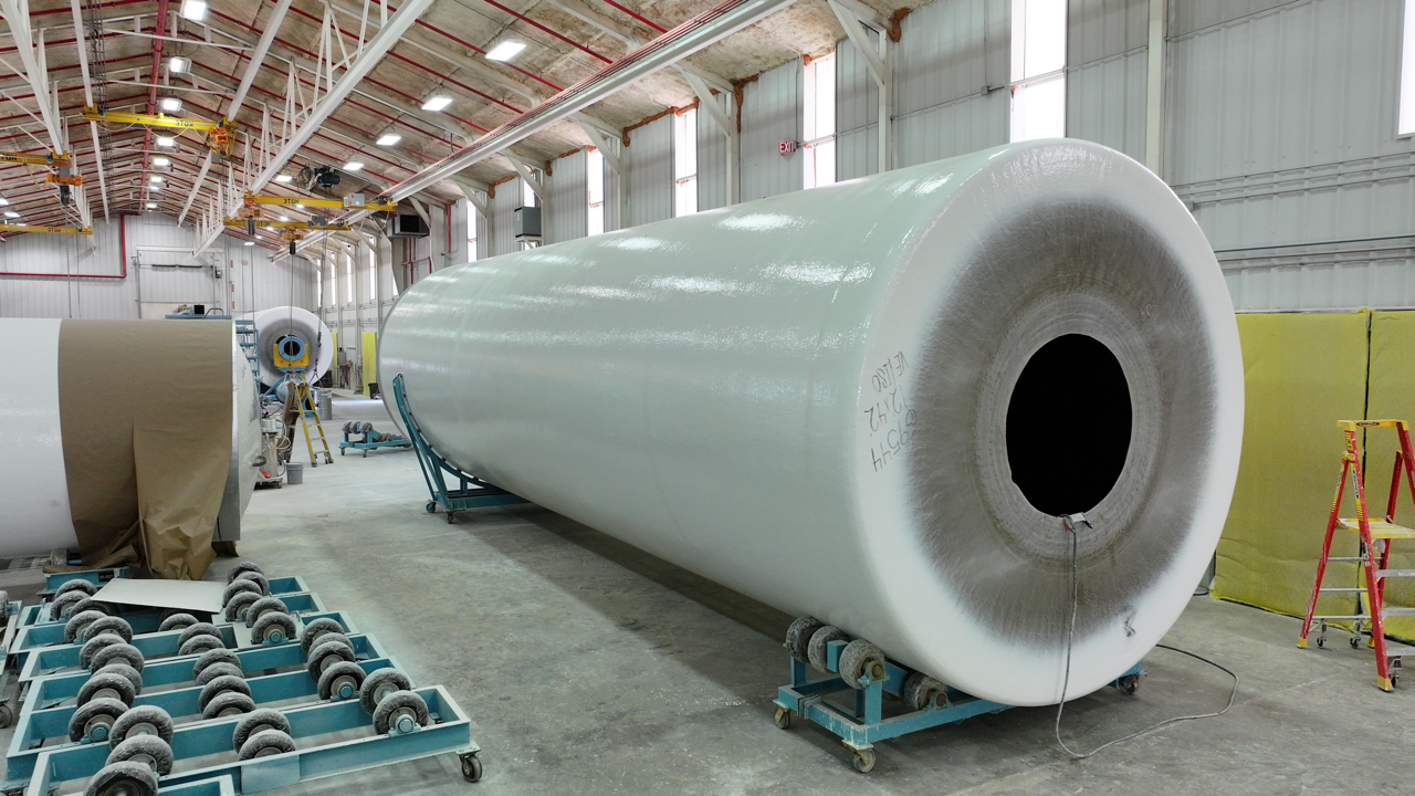 Large white cylindrical object inside a factory, resting on blue supports.