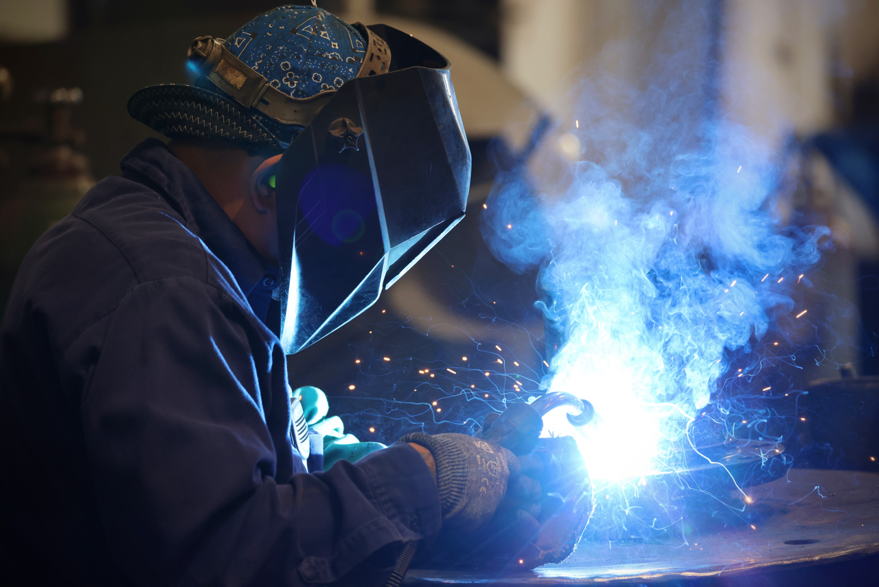 Welder in blue protective gear welds, producing bright sparks and light.