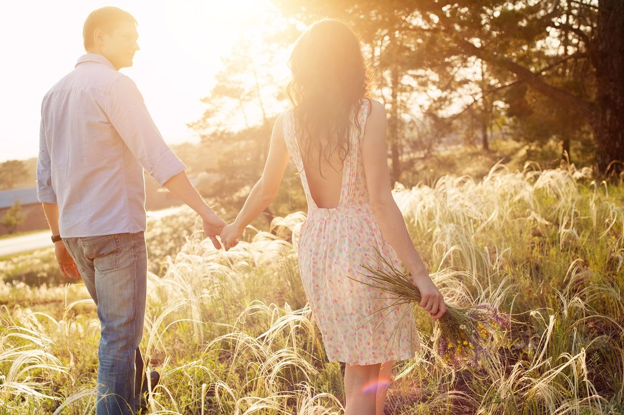 A man and a woman are walking through a field holding hands.
