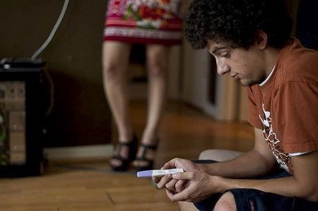 A man is sitting on the floor holding a pregnancy test.