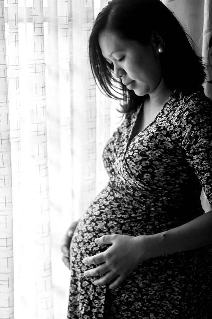 A pregnant woman is standing in front of a window holding her belly.