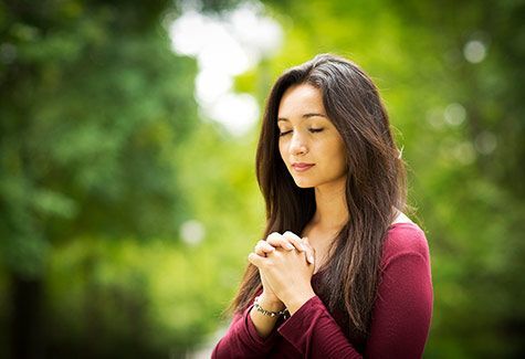 A woman is praying with her eyes closed in a park.