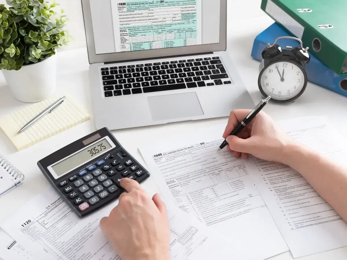 Person calculating numbers and completing forms on a laptop while working on direct bill in insurance.