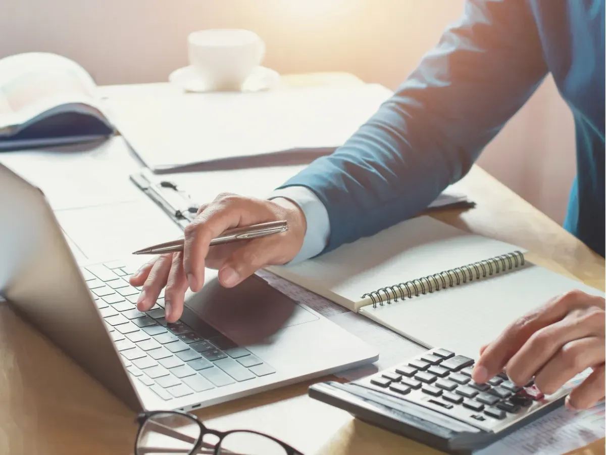 Person using a laptop and calculator at a desk, showing the need to hire a bookkeeper.