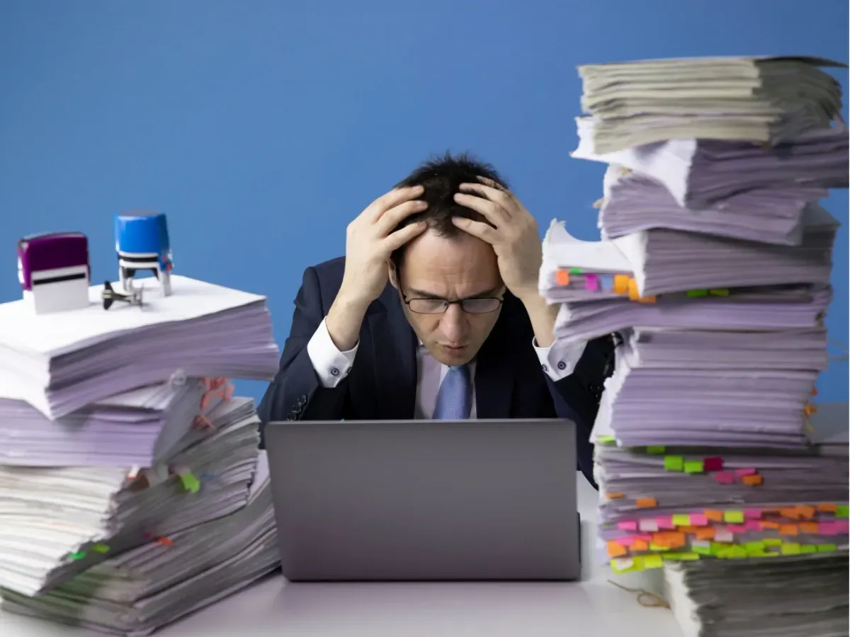 Stressed man surrounded by paperwork, showing why it’s time to hire a bookkeeper.