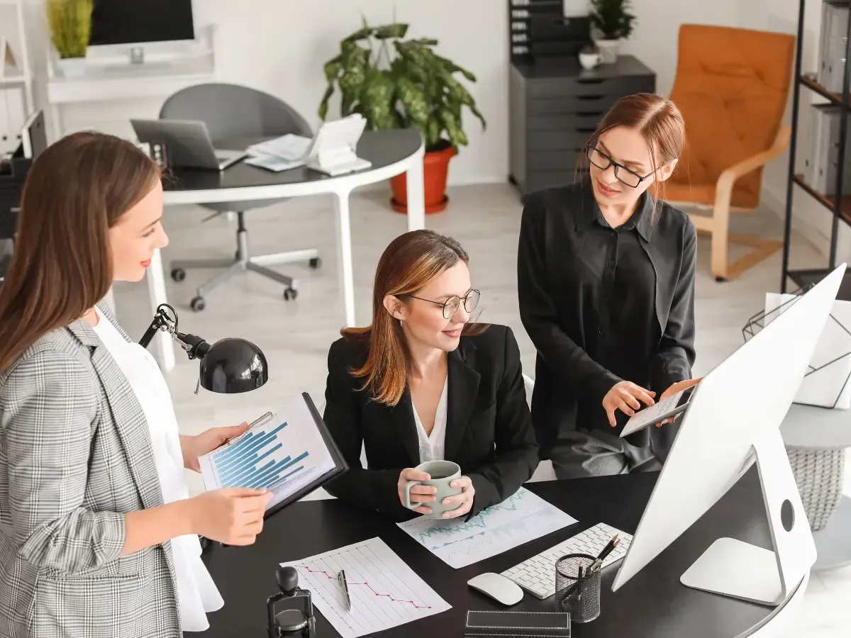 Three professionals reviewing charts at a desk during insurance bookkeeping work in a modern office