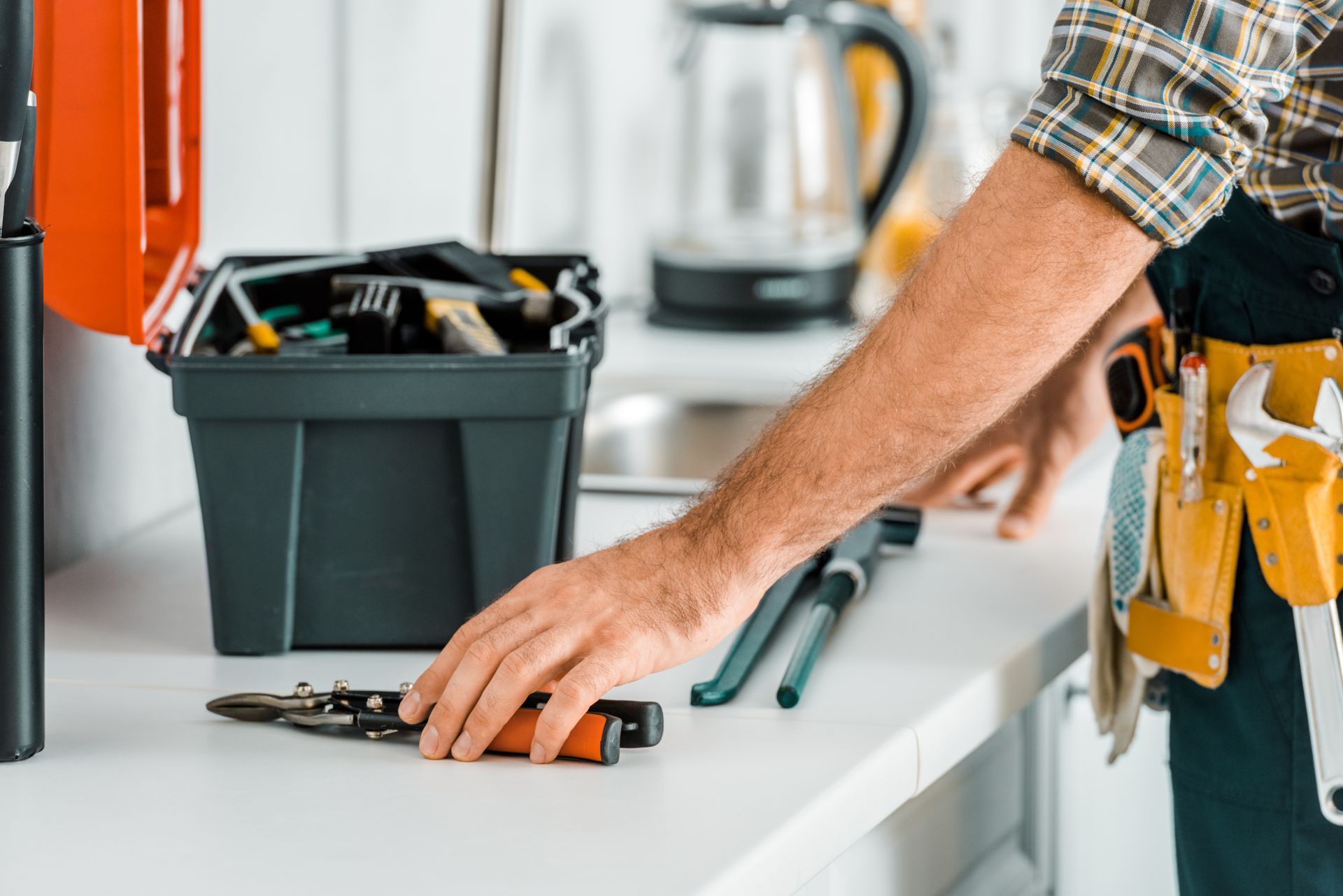 Hand reaching for pliers on a kitchen counter, with an open toolbox nearby.