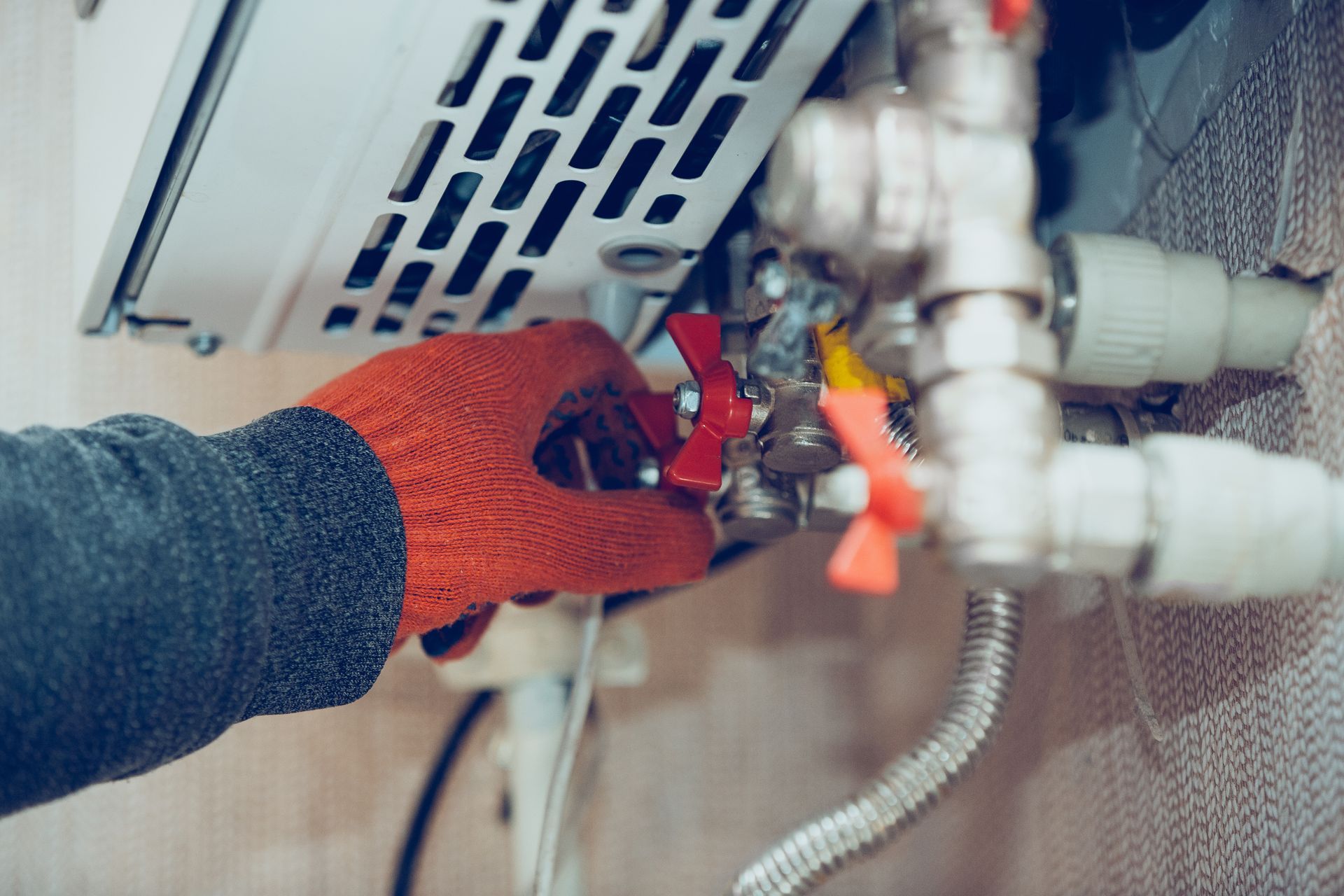 Gloved hand tightening plumbing valves beneath a sink with exposed pipes Gloved hand tightening plumbing valves beneath a sink with exposed pipes