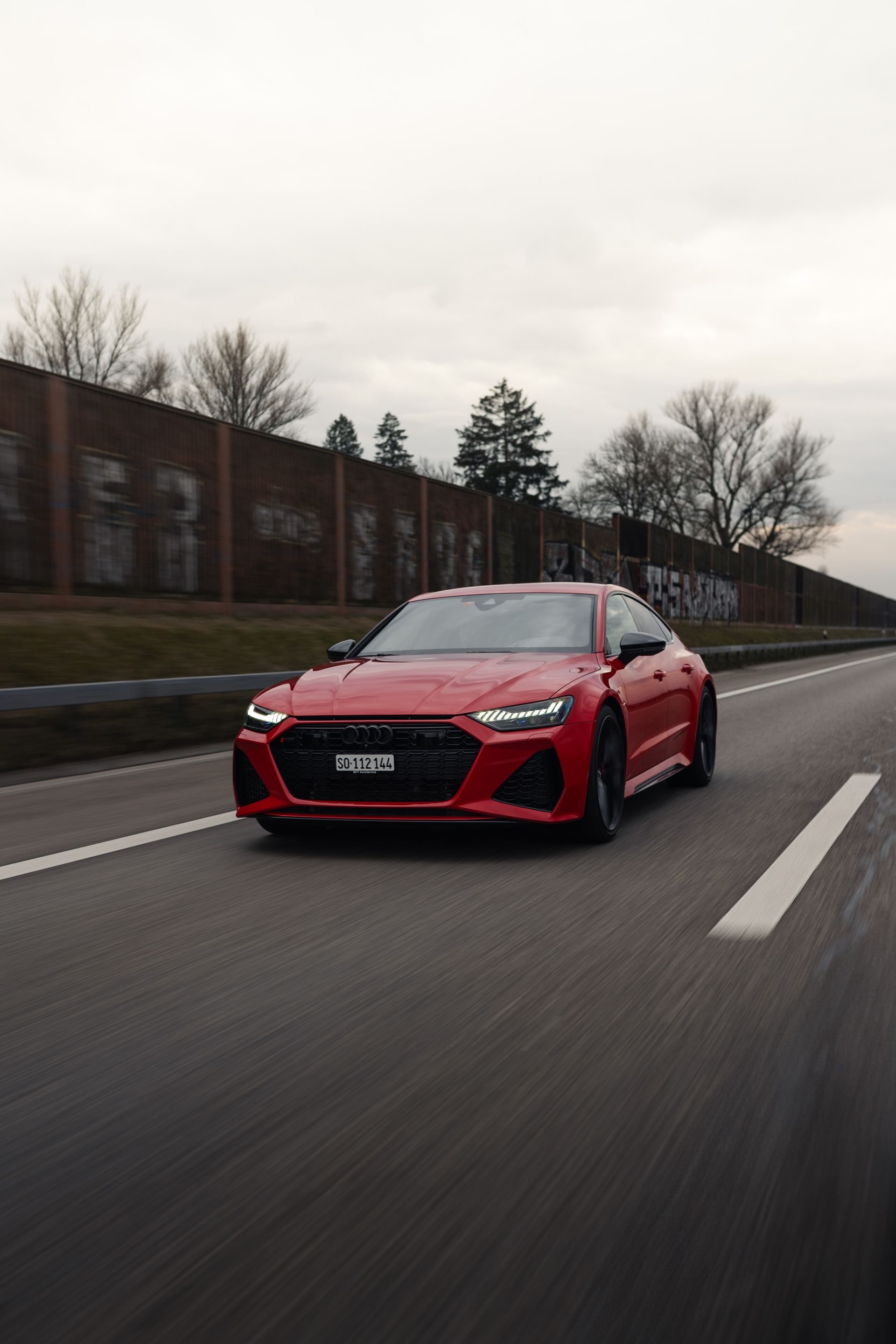 Ein rotes Auto fährt auf einer Autobahn neben einem Zug her.