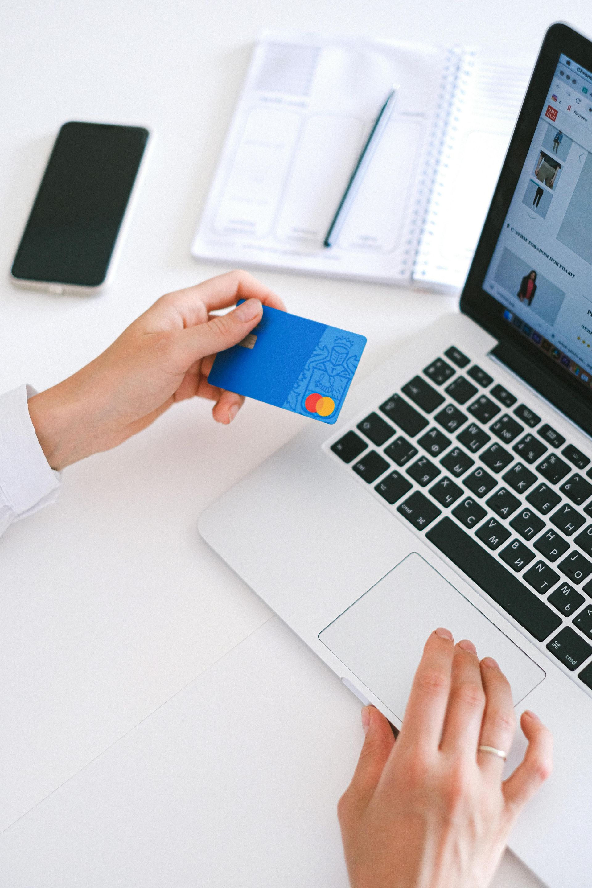 Person holding a blue credit card near a laptop during an online purchase