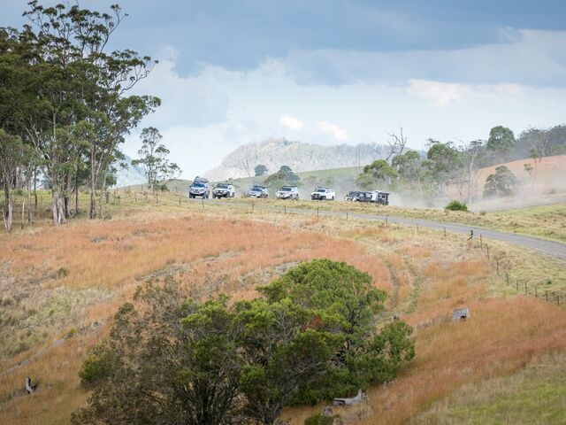 Cars Driving Down a Dusty Road Through a Grassy, Hilly Landscape Under a Cloudy Sky — Lacey's TJM 4X4 Megastore in Central Queensland, QLD