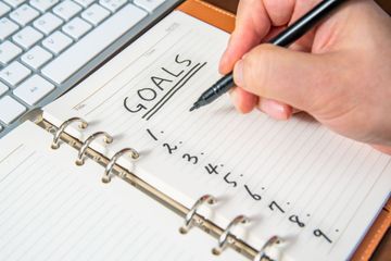 A person is writing goals in a notebook with a pen