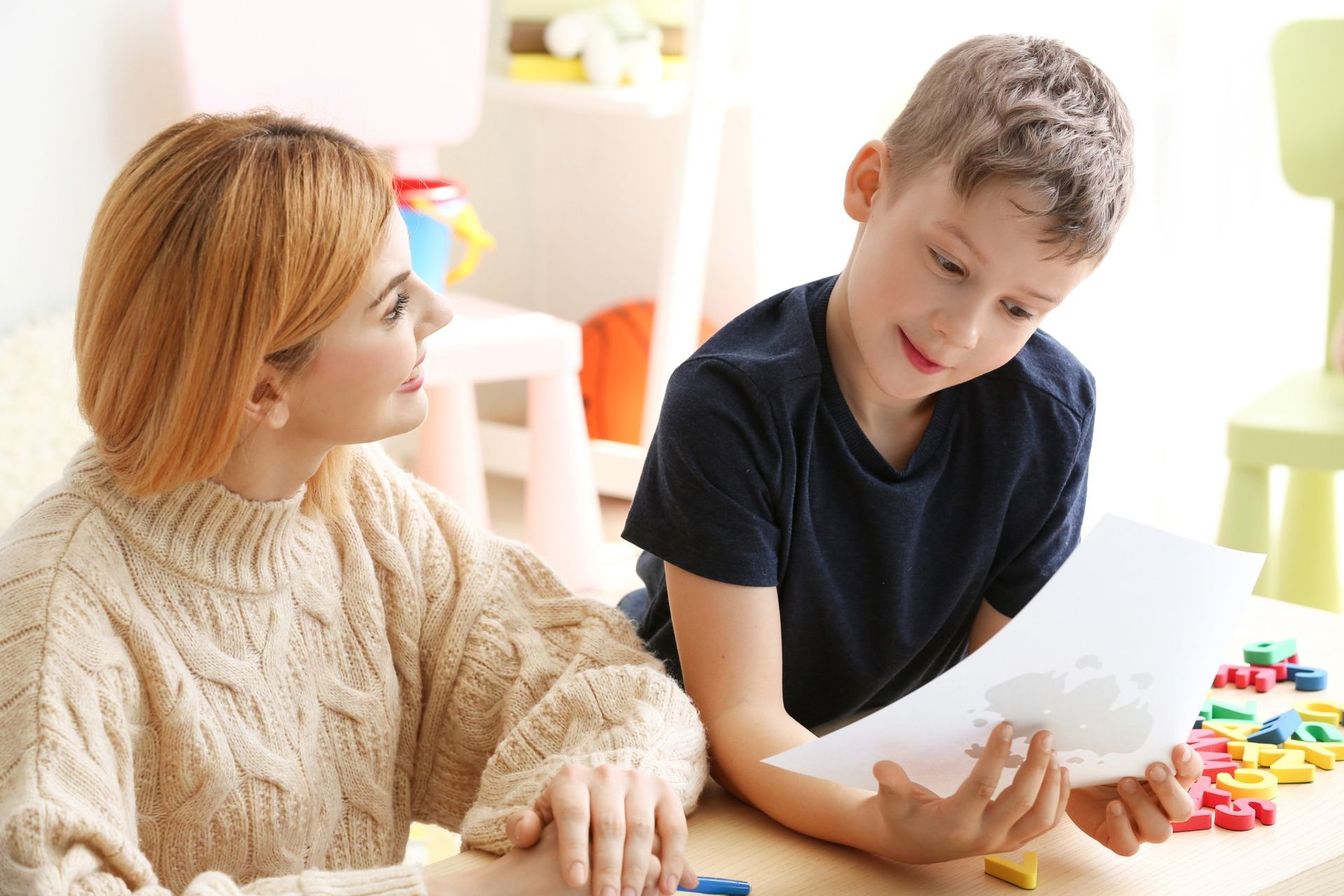 Woman and child looking at paper together at a table with colorful blocks.