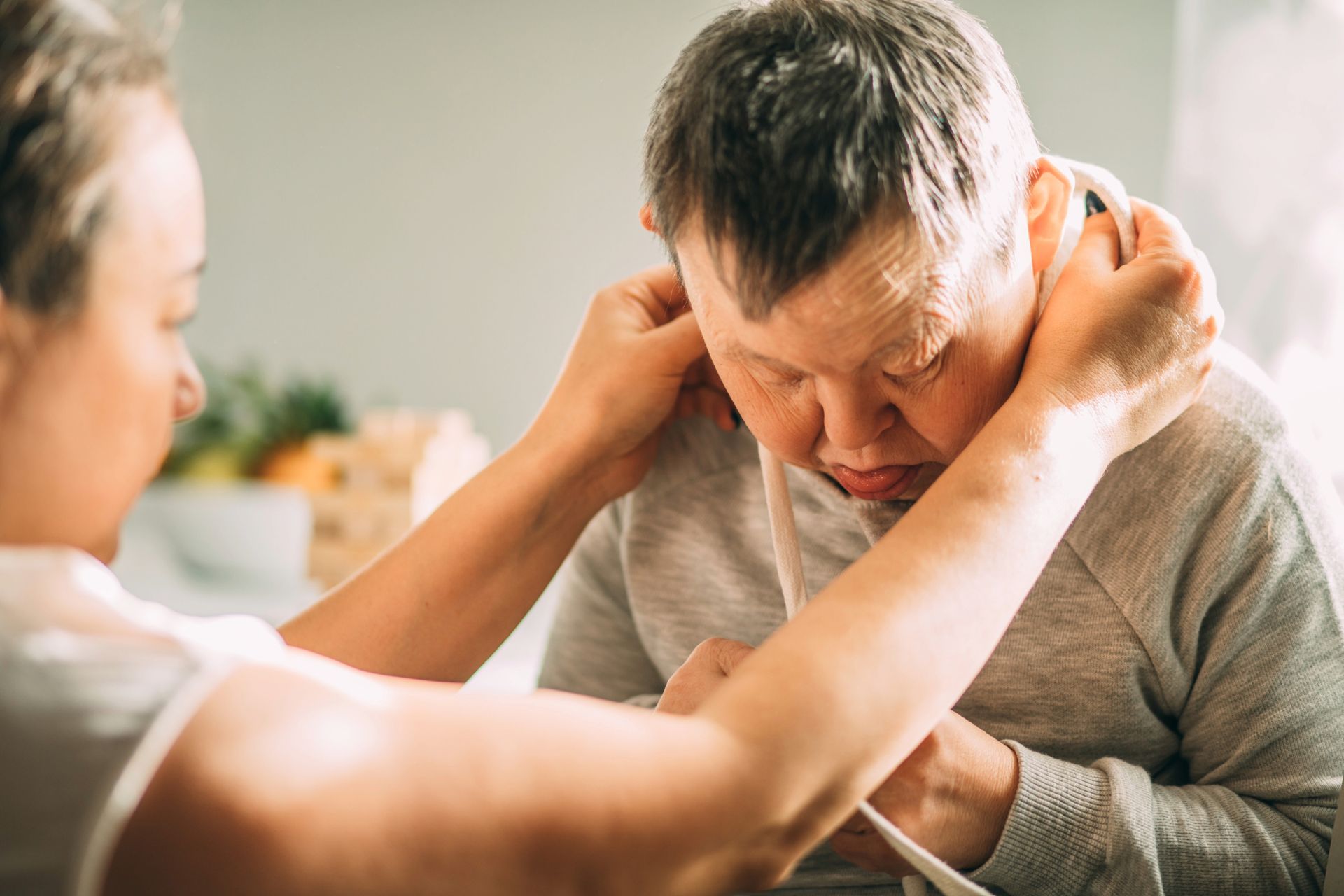 Person adjusting a caregiver's clothing, assisting a person with Down syndrome indoors.
