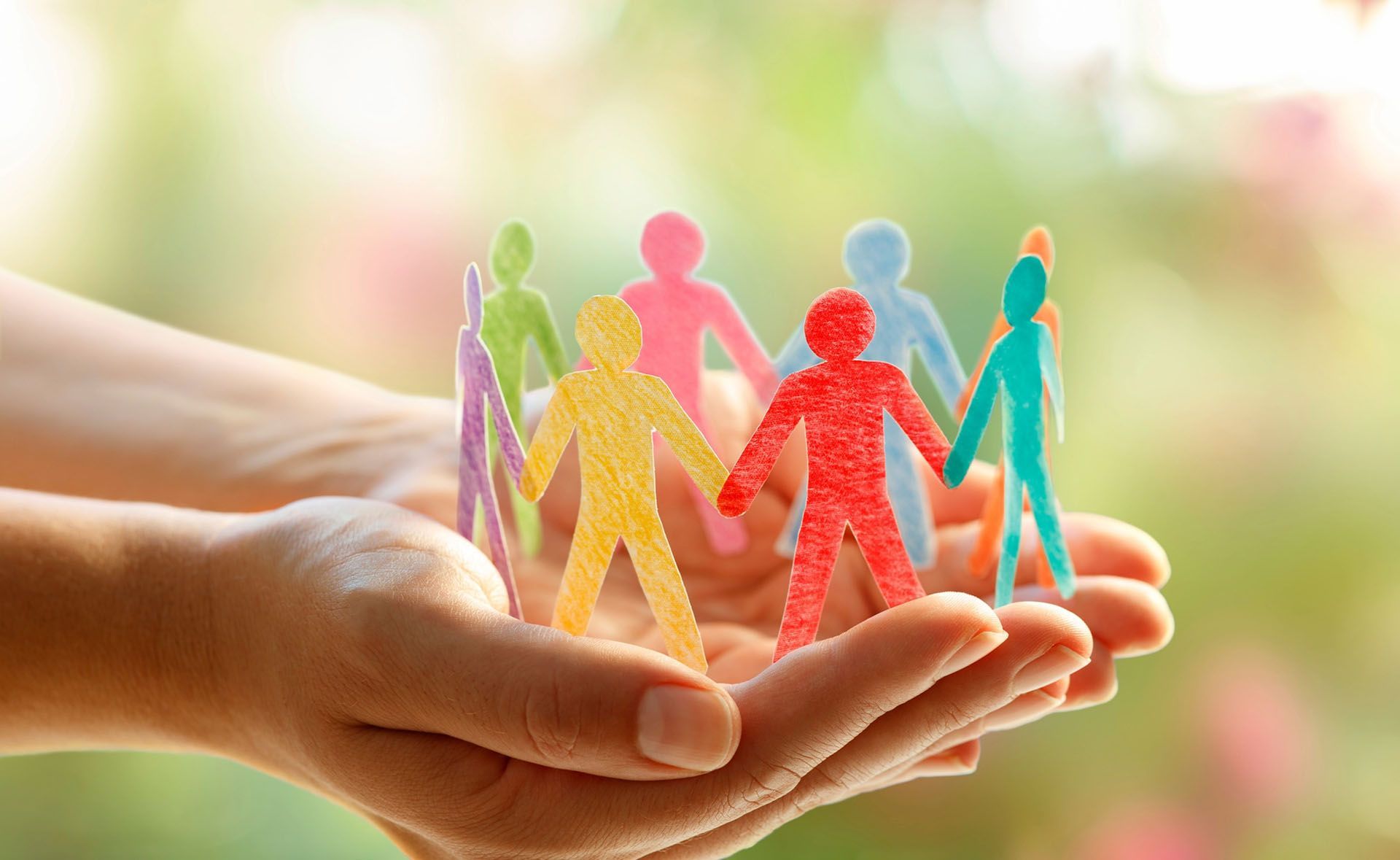 Hands cupping colorful paper cutouts of people.