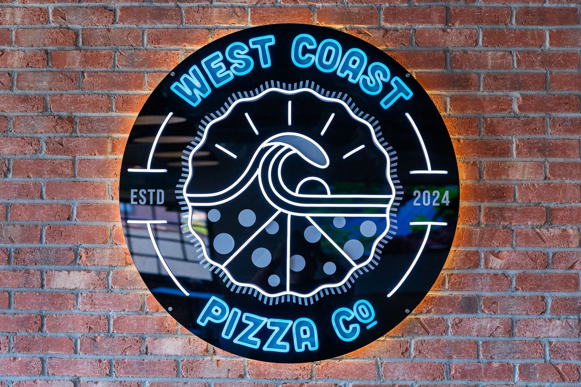A sign for west coast pizza co. on a brick wall