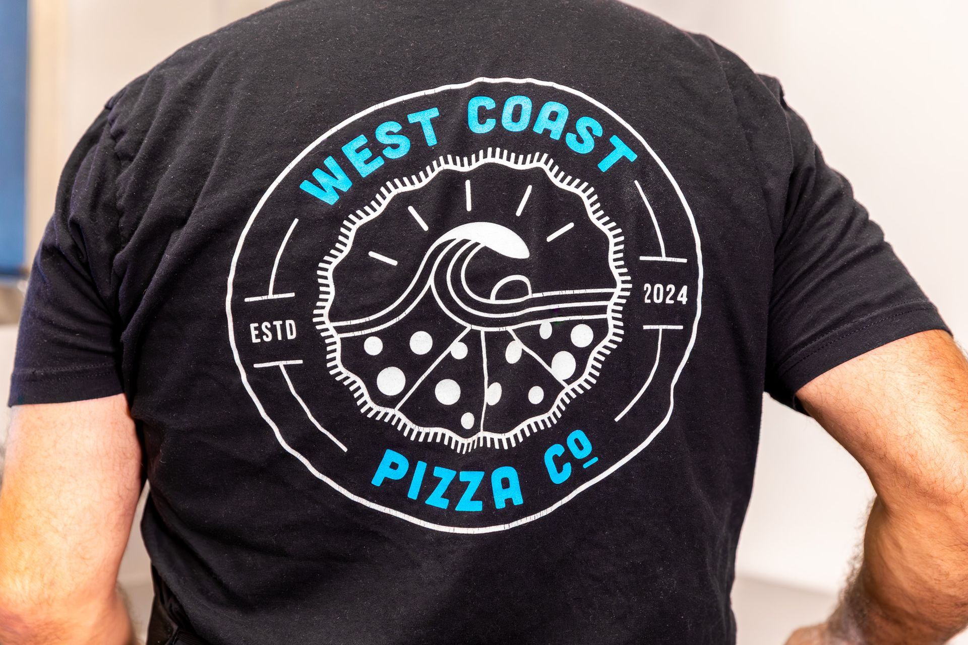 The back of a person wearing a west coast pizza co. t-shirt