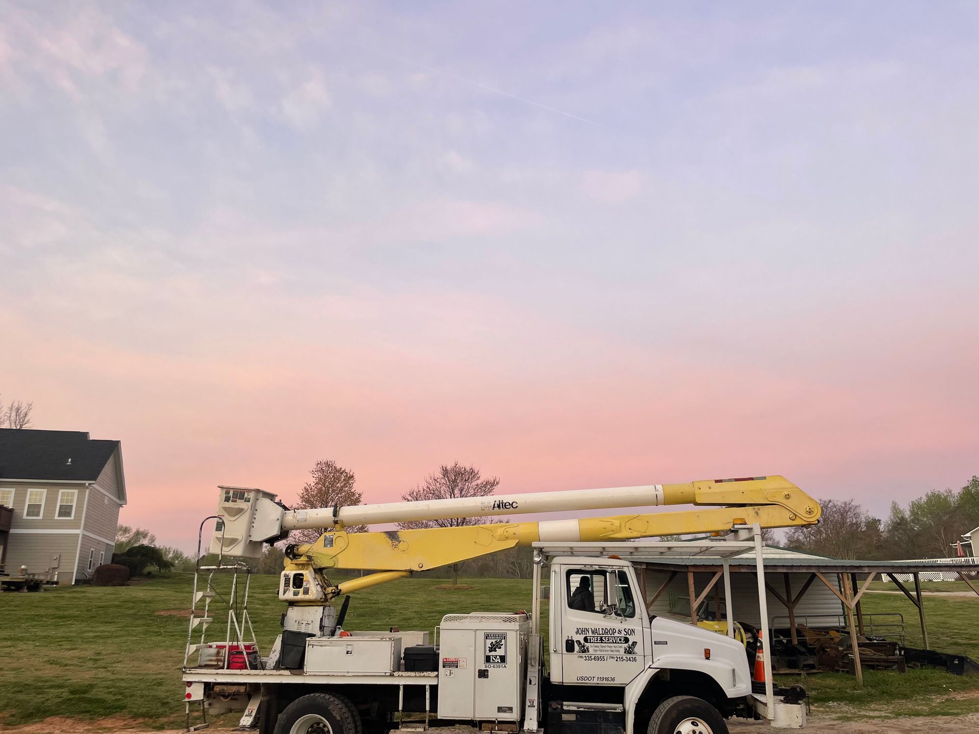 White utility truck with extended boom under a pastel sky.