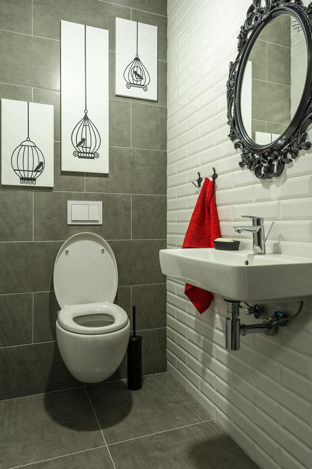 Modern bathroom with gray and white tile, toilet, sink, mirror, and red towel.