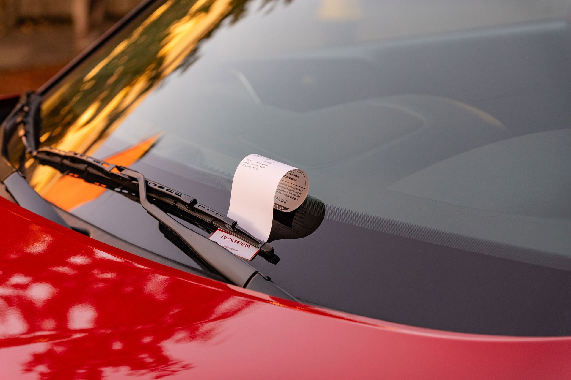 A red car with a parking ticket on the windshield.