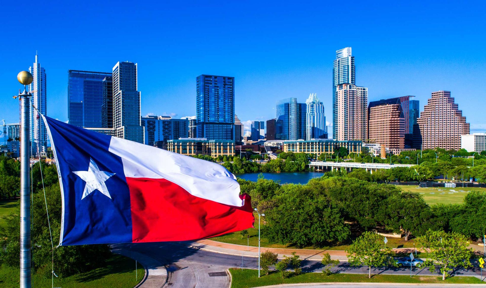 A Texas flag is waving in the wind in front of a city skyline.