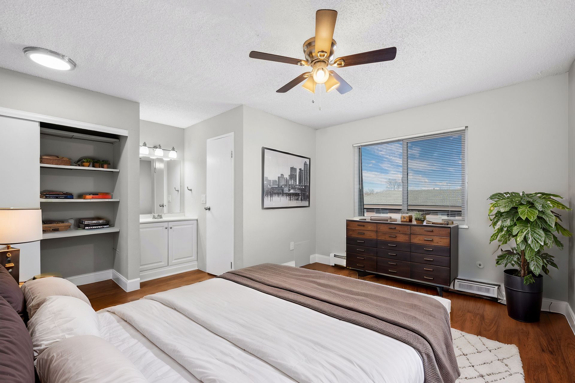 Photo of a bedroom with built-in shelving in the closet and an area near a bathroom with a vanity mirror