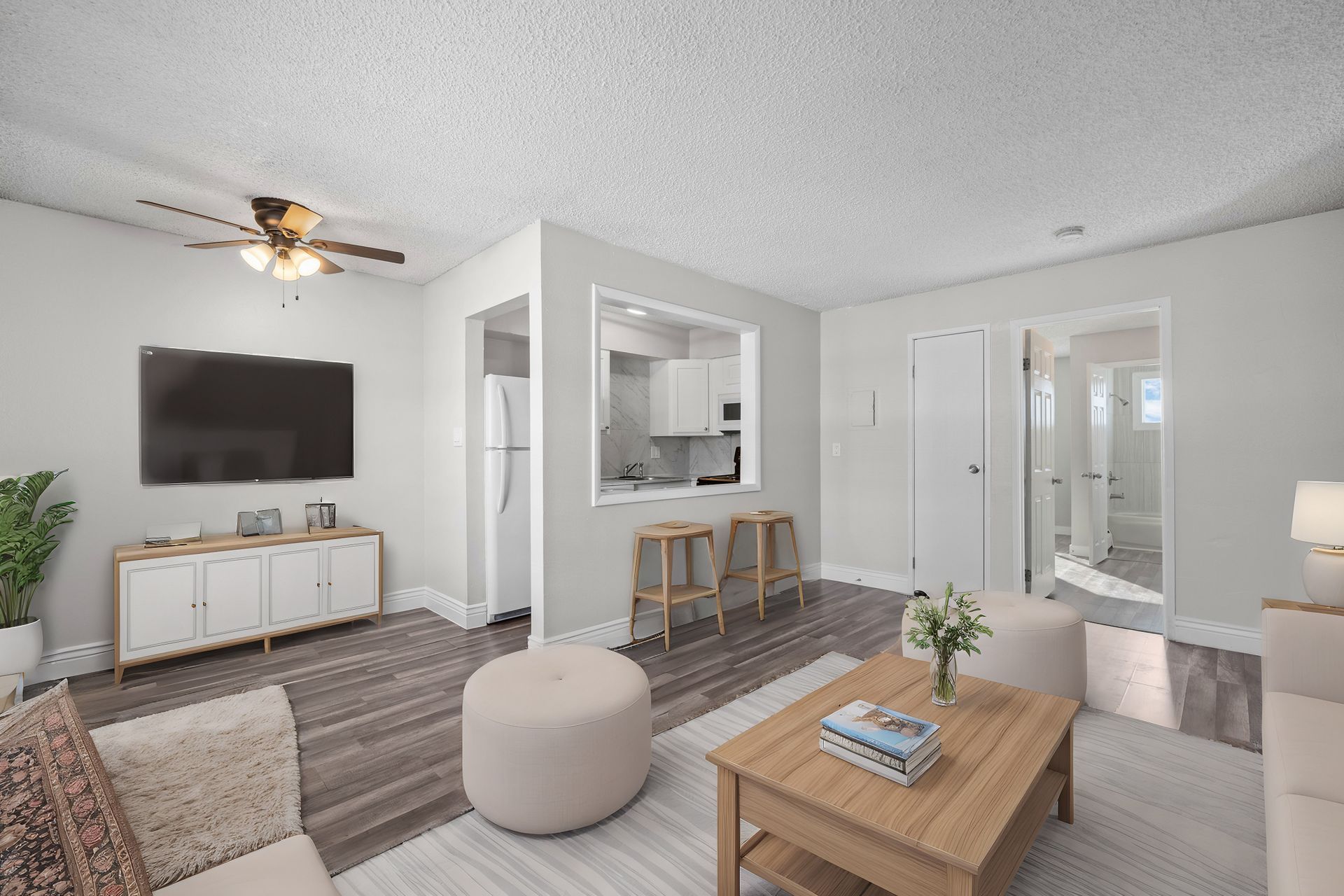Photo of a living room with a ceiling fan, small kitchen and a bathroom in the background