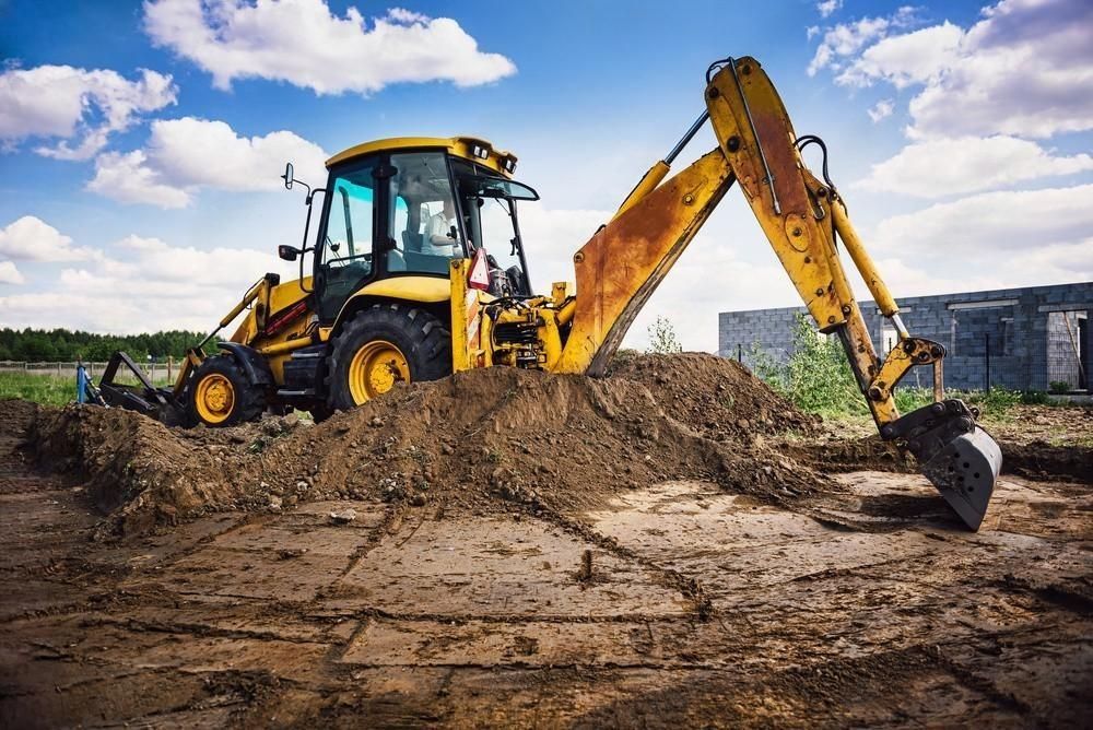 A yellow excavator is digging a hole in a dirt field.