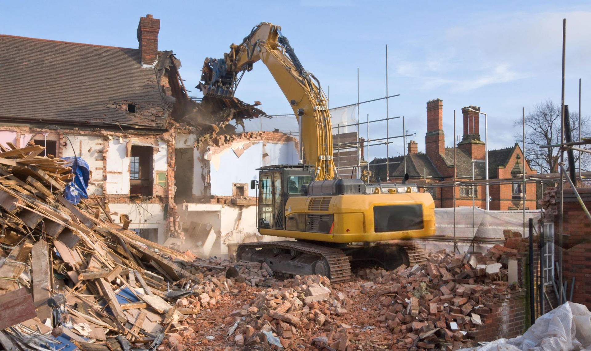 a yellow excavator is demolishing a brick building