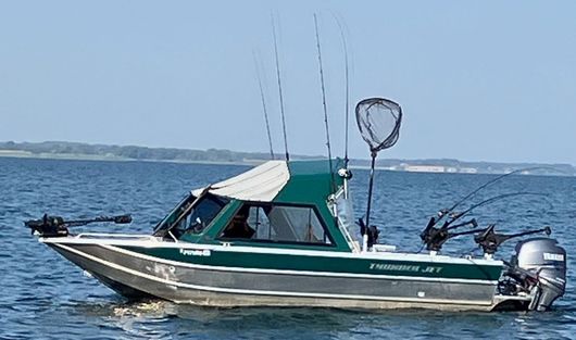 A green and silver boat is floating on top of a body of water.