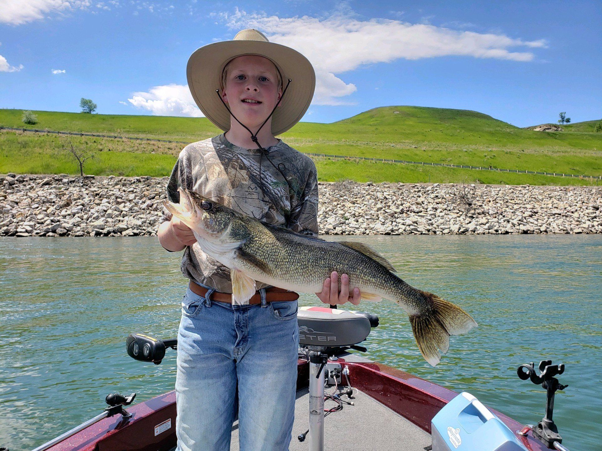 A young boy is standing on a boat holding a large fish.