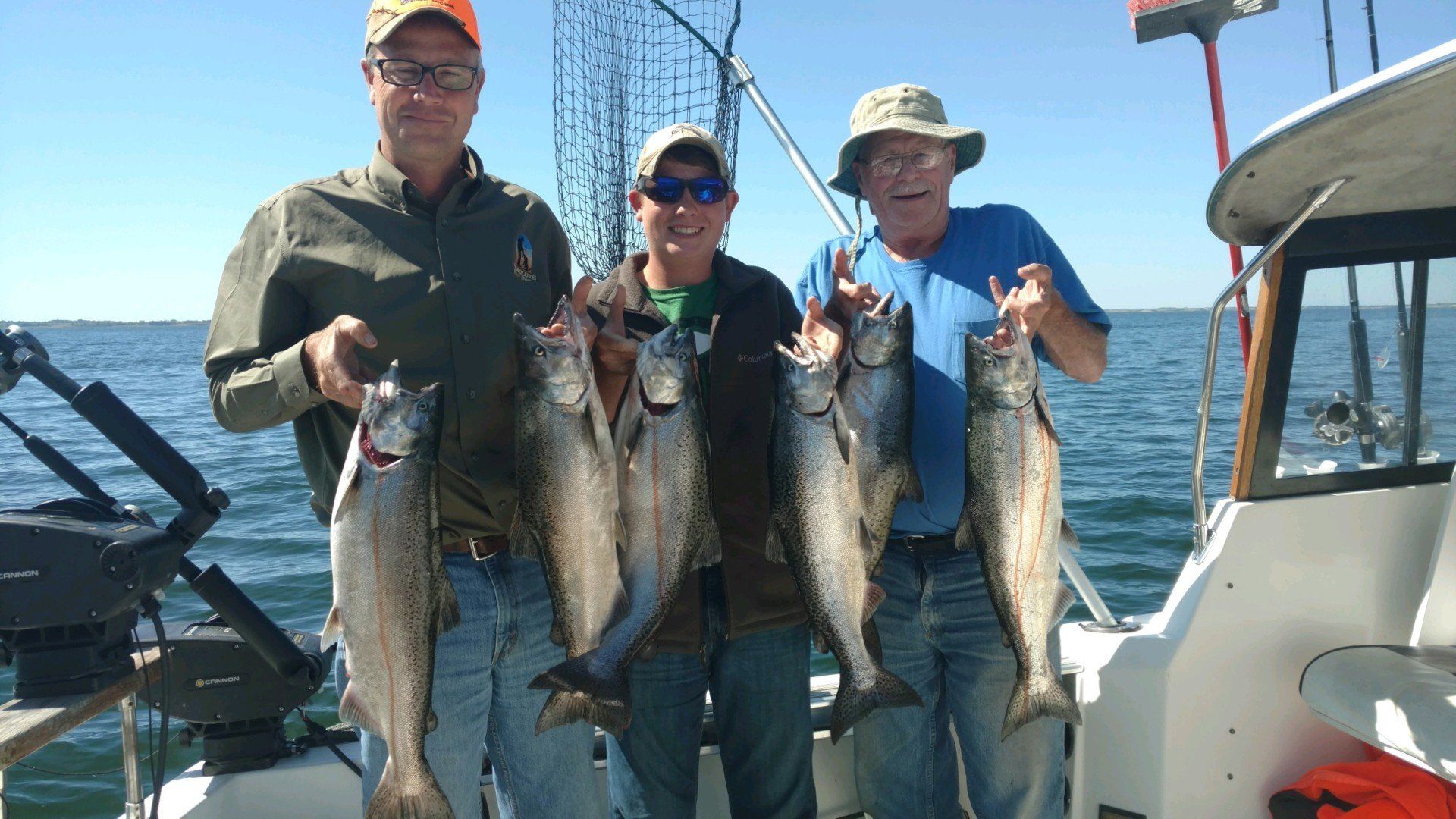 Three men are standing on a boat holding fish