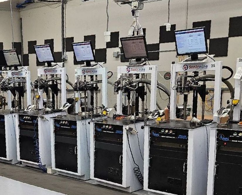 Rows of Sonic Nozzle Provers with computer screens, likely for manufacturing or testing in a factory setting.