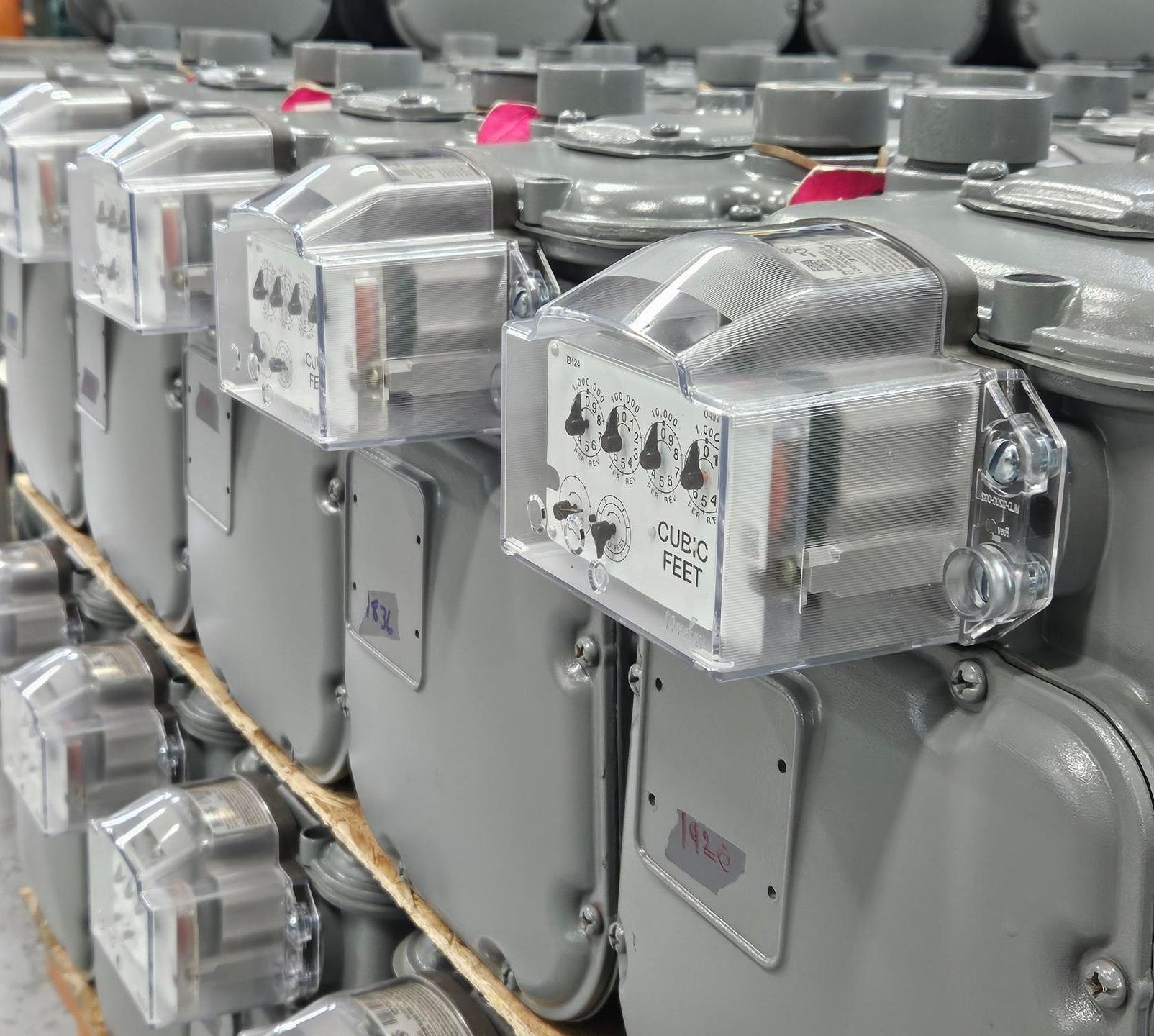 Close-up of a row of gray gas meters with transparent covers, likely in a warehouse setting.