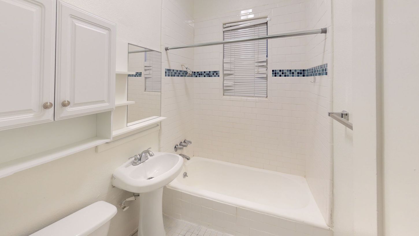 Bathroom with a white pedestal sink, tub, toilet, and cabinet, all against white walls.