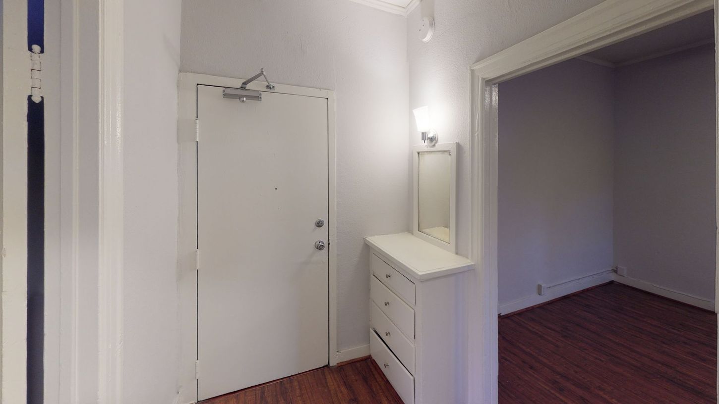 Entryway with white door, dresser, mirror, and hardwood floor.