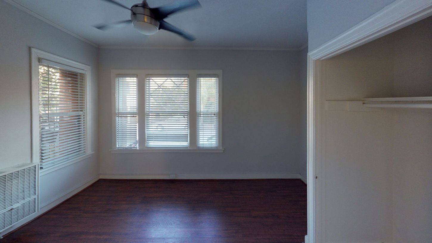 Empty room with windows, dark wood floor, white walls, and closet.