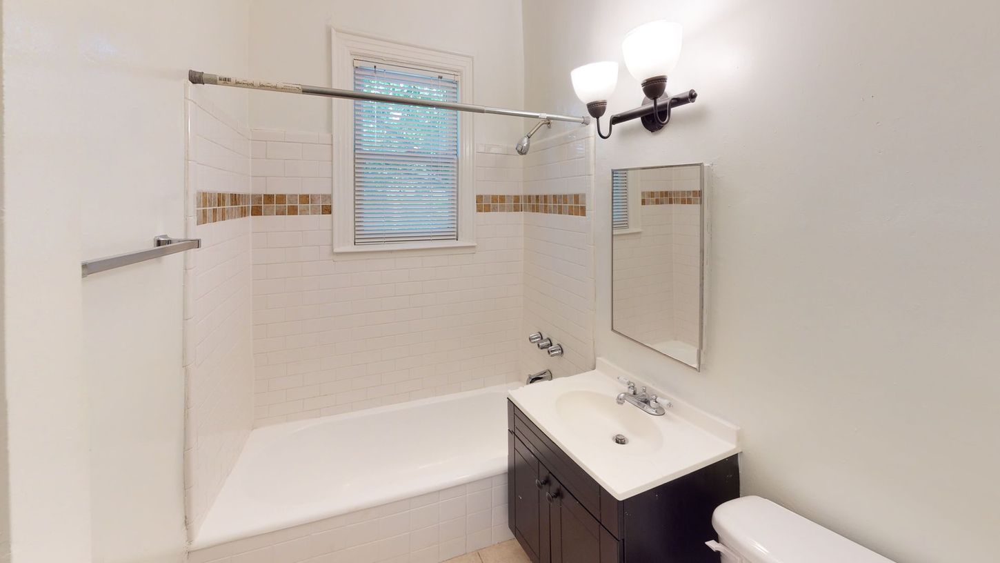 Bathroom with white tiles, bathtub, sink, toilet, and a window.