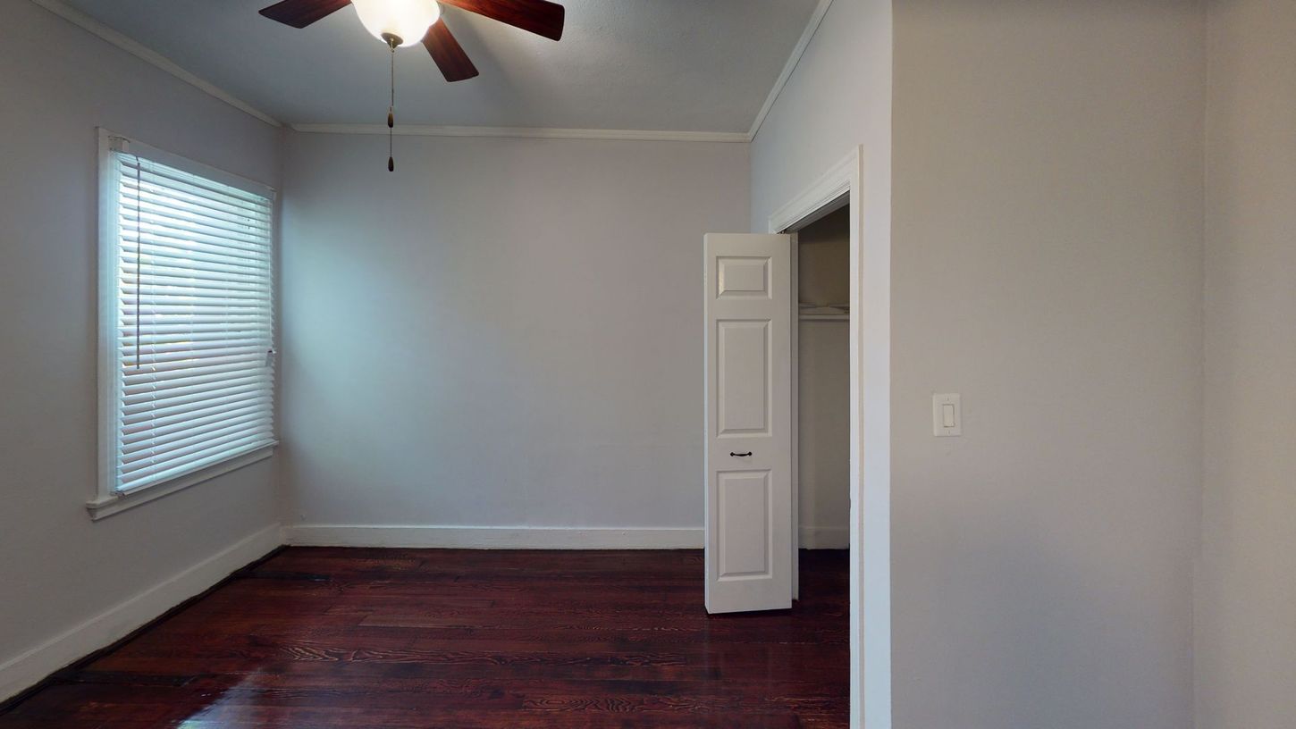 Empty bedroom with dark wood floors, a window with blinds, and a white door.