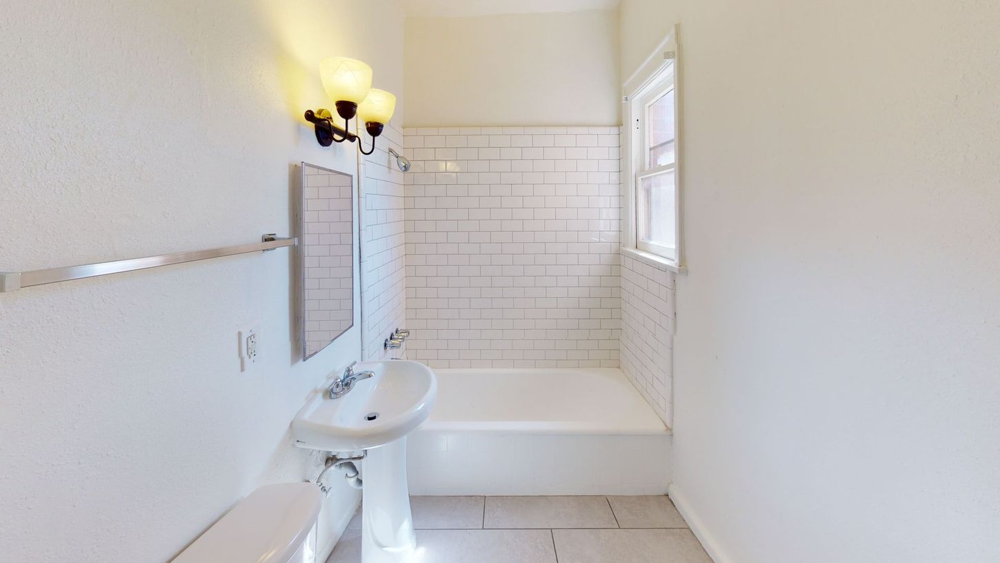 Bathroom with white subway tile shower, pedestal sink, and window.