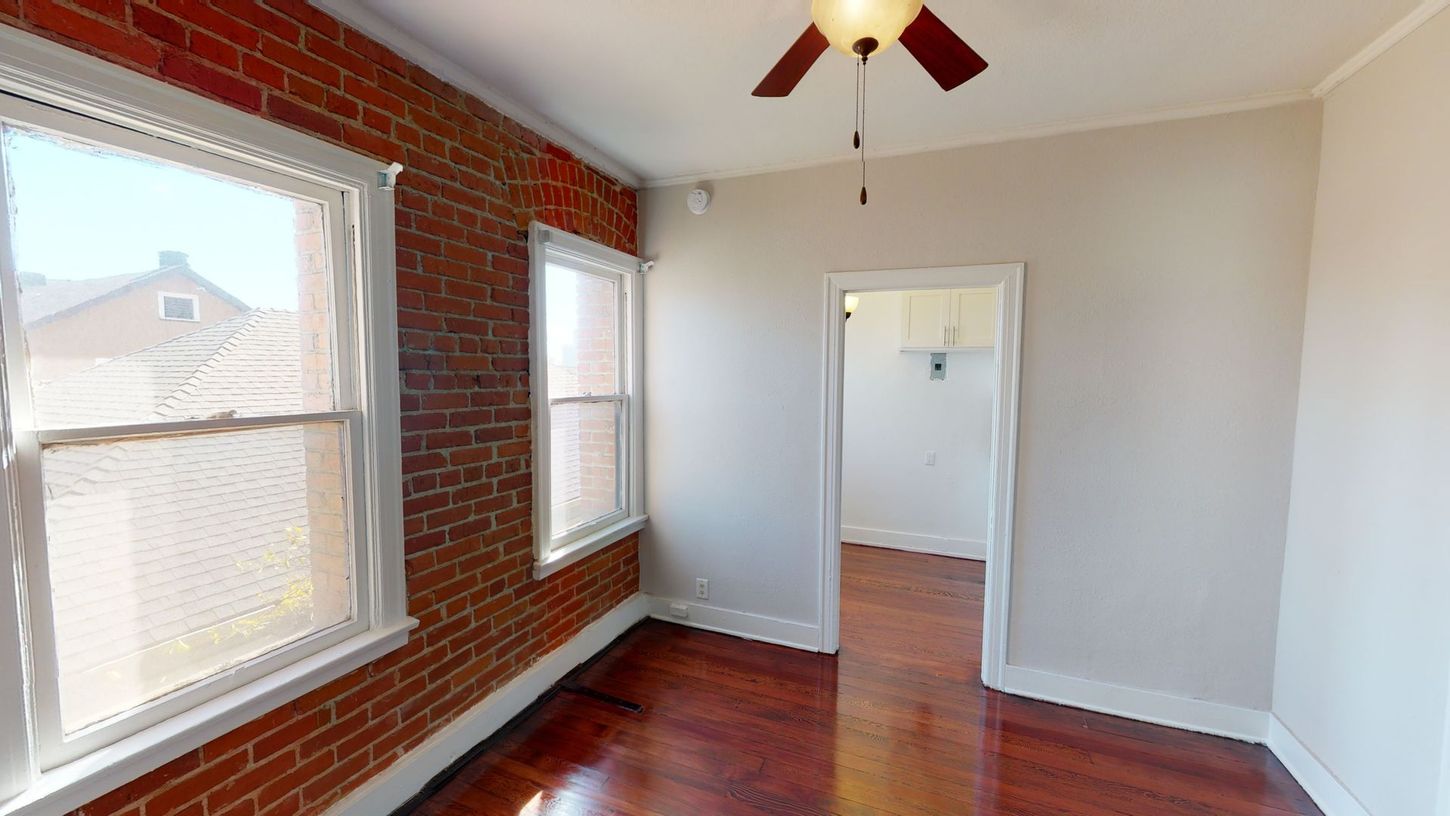 Interior room with exposed brick wall, windows, wooden floor, and a doorway.