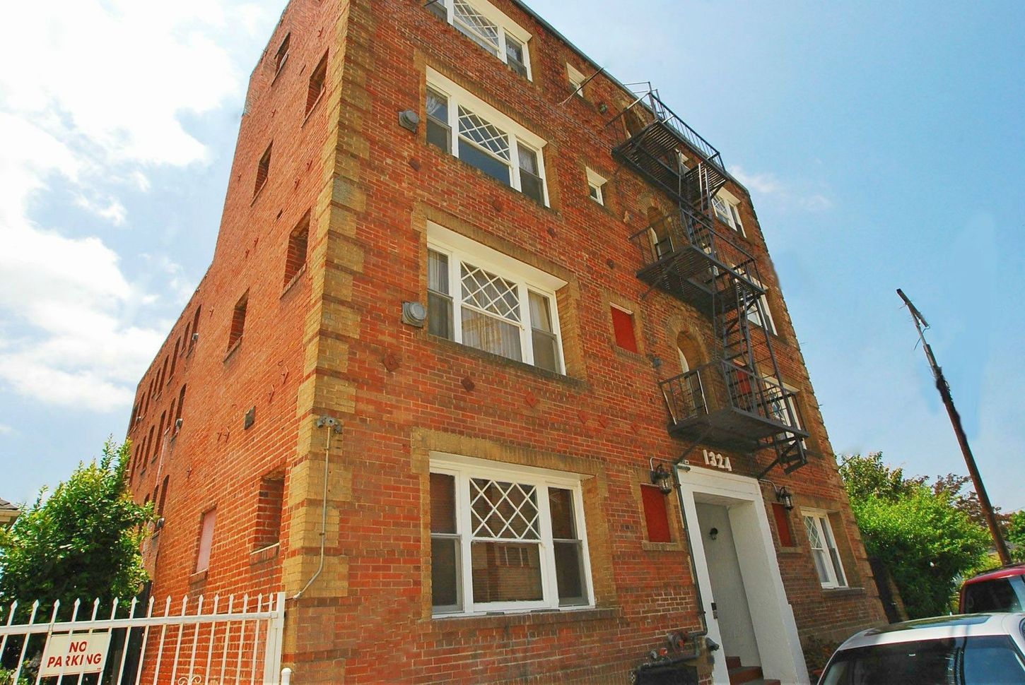 Brick apartment building with fire escape, white trim, and a white fence.